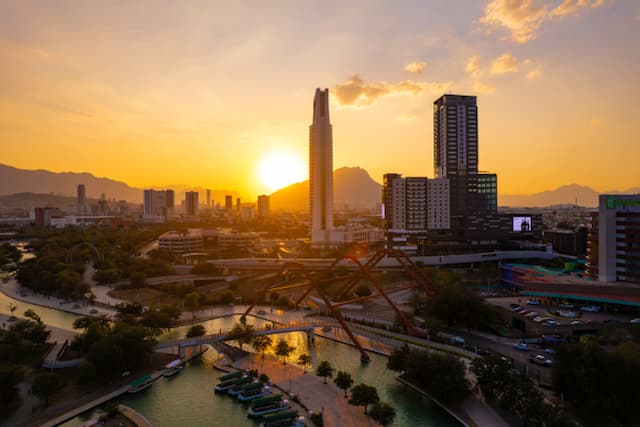 Vista de la ciudad al atardecer con un canal, edificios altos y montañas al fondo