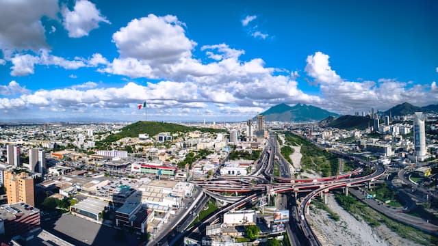 Vista panorámica de una ciudad con un paisaje montañoso al fondo y un cielo despejado con nubes.