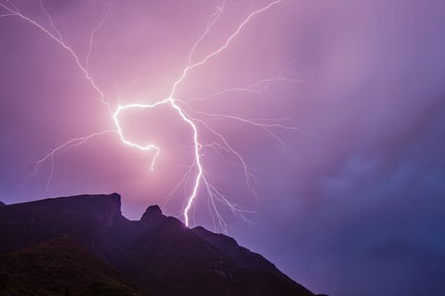 Rayo iluminando el cielo nocturno sobre una formación montañosa